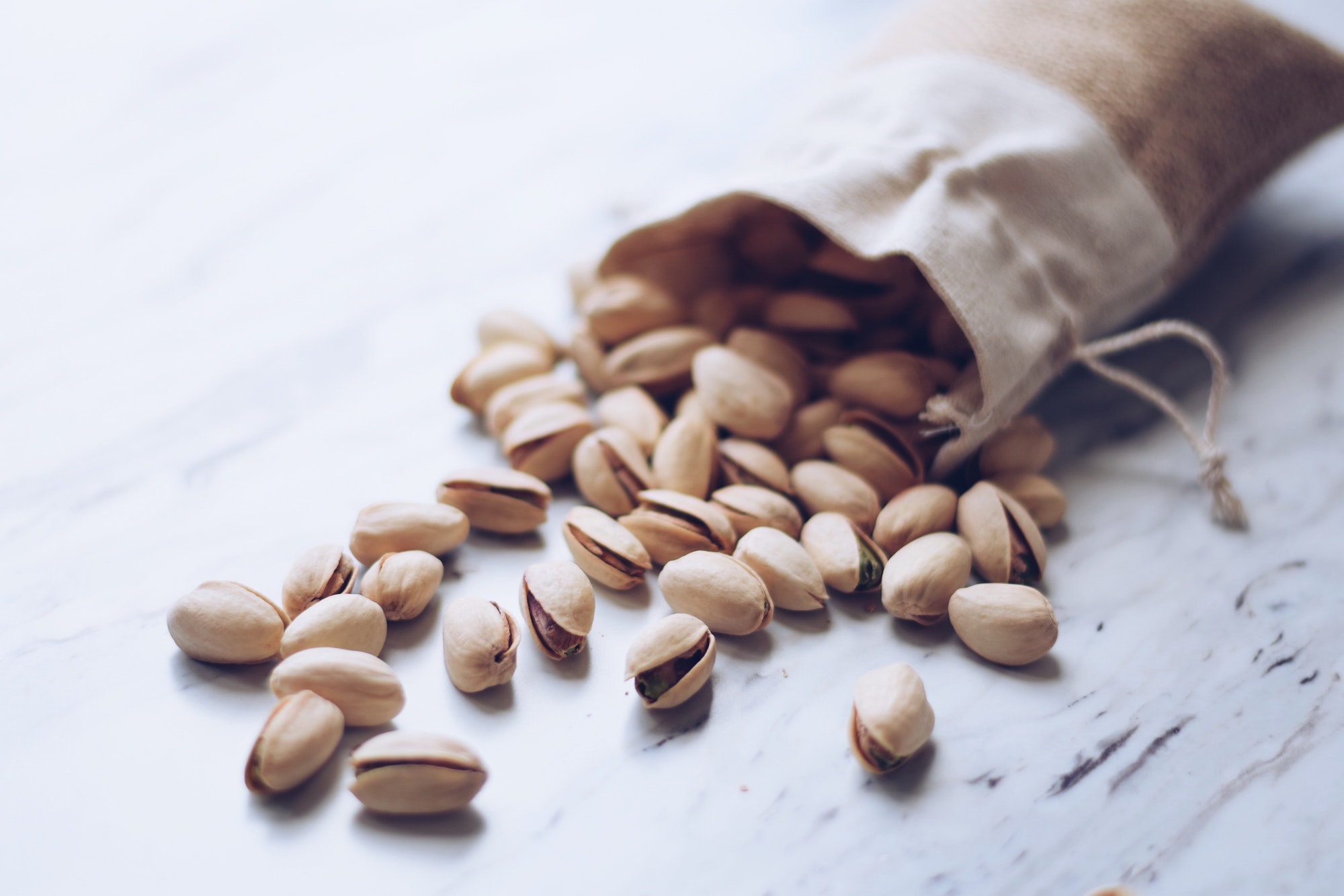 Pistachio nuts spilling out of a natural linen bag on a marble countertop